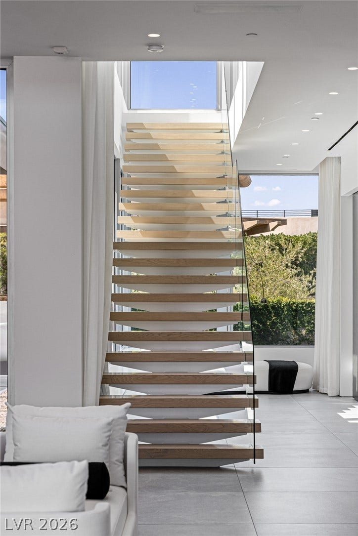 A striking modern staircase with glass railing creates a focal point in this sun-drenched interior.
