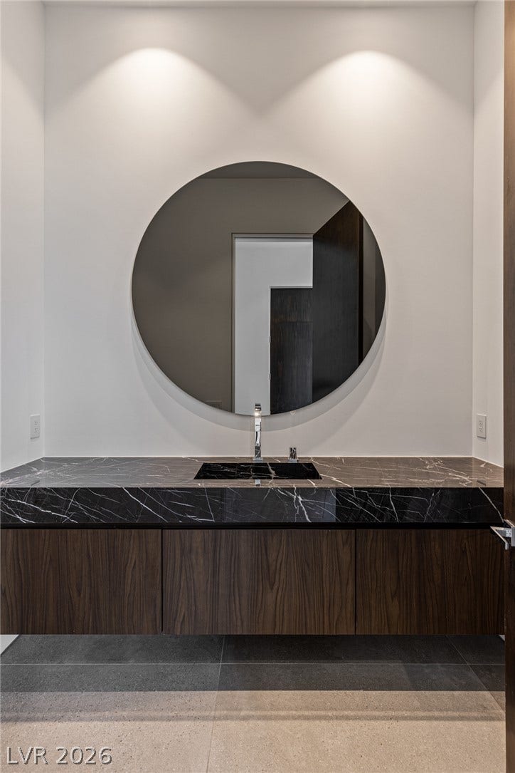 A sleek powder room presents a floating wood vanity with a black marble countertop and round mirror.