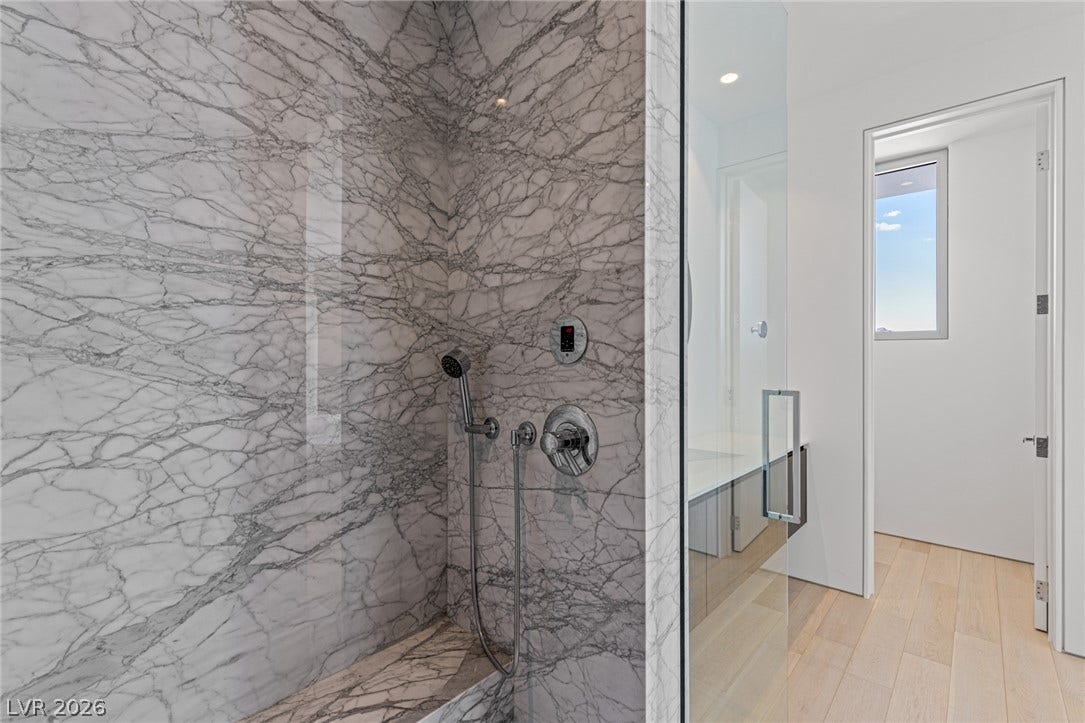 Marble-clad shower features sleek fixtures and a spacious design, seamlessly blending luxury with functional elegance.