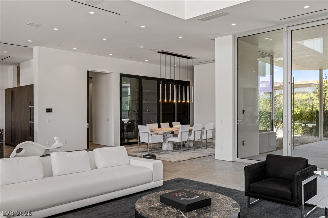 An open-concept interior features floor-to-ceiling glass doors, revealing an inviting outdoor oasis.