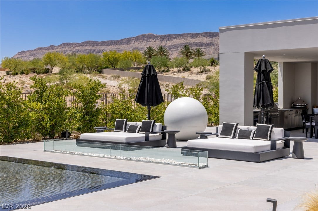 An inviting pool area with stylish lounge beds awaits, framed by rugged desert mountains and verdant landscaping.