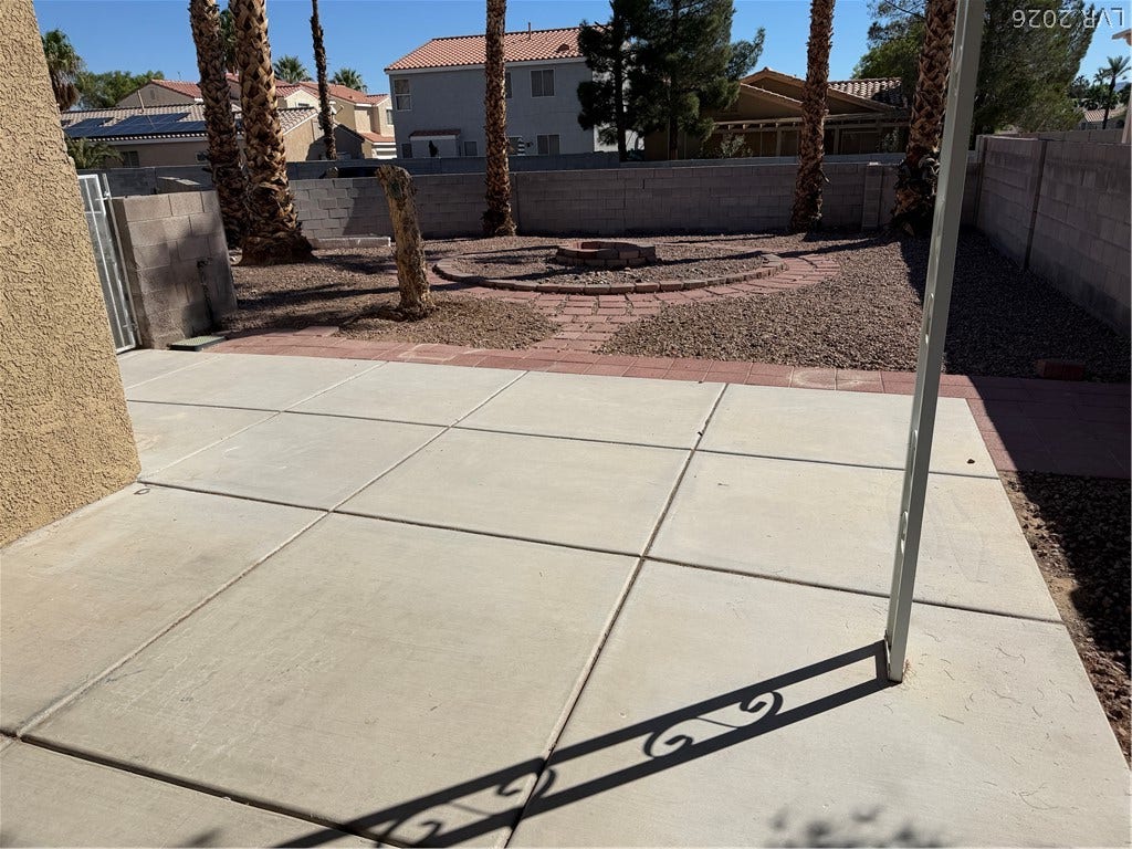 An expansive concrete patio overlooks a low-maintenance gravel yard enclosed by a block wall.