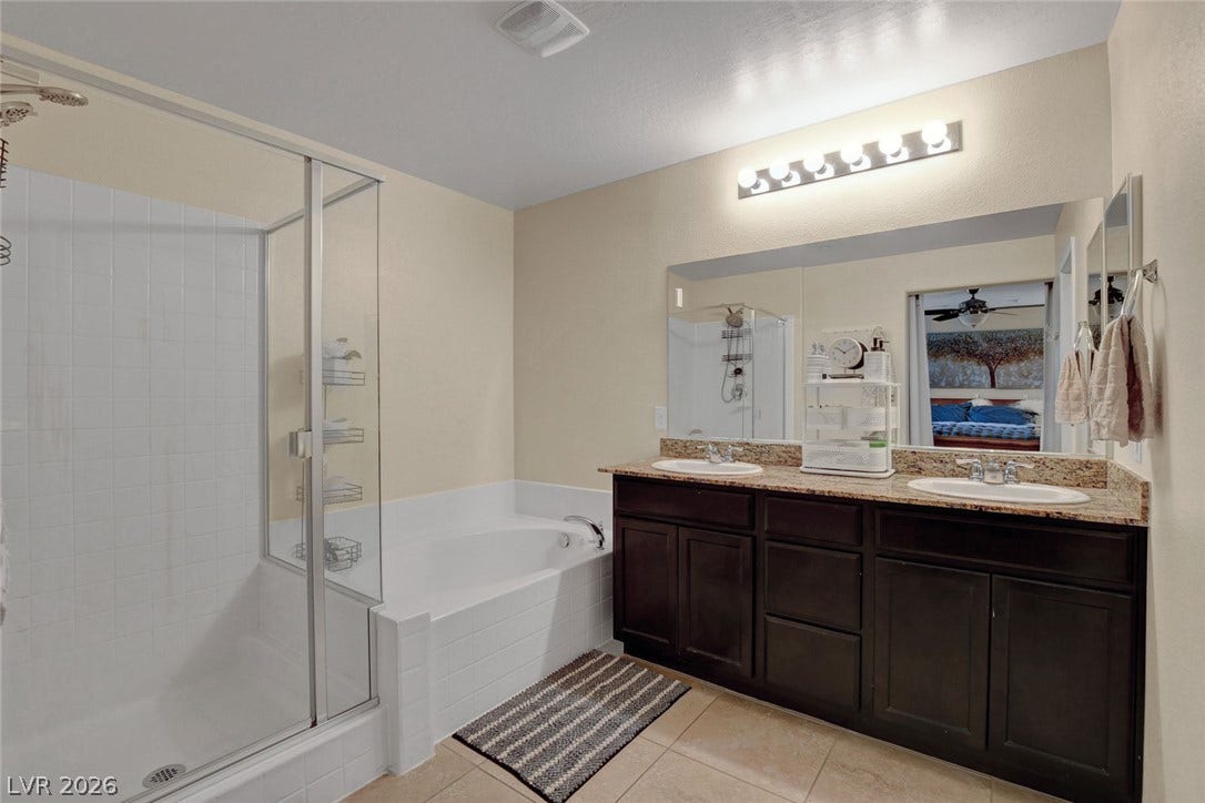 3924 Juanita May Avenue, North Las Vegas, NV 89032 Double vanities with stone countertops stand alongside a glass-enclosed shower and adjacent soaking tub.