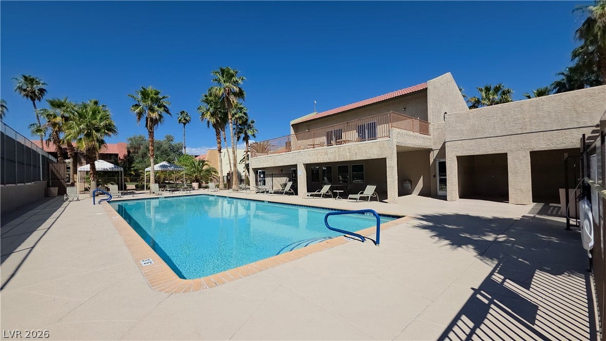 4470 Sandy River Drive, #54, Las Vegas, NV 89103 A sparkling swimming pool sits adjacent to a sun-drenched clubhouse patio lined with palm trees.