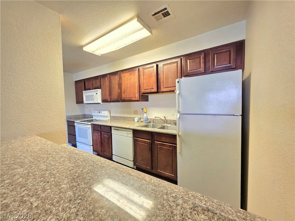 4470 Sandy River Drive, #54, Las Vegas, NV 89103 Rich wood cabinetry contrasts with neutral stone counters in this functional cooking space.