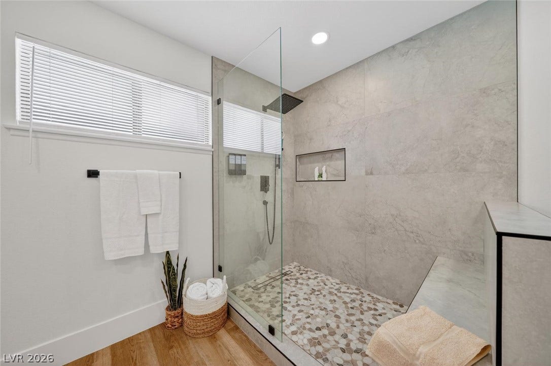 6191 Bullion Boulevard, Las Vegas, NV 89103 Large glass-enclosed shower showcases stone tile accents and a built-in bench.