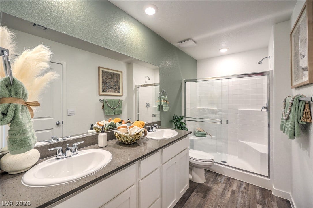 923 Black Heron Street, Henderson, NV 89011 Double vanities with stone counters flank a glass-enclosed walk-in shower in this modern bathroom.