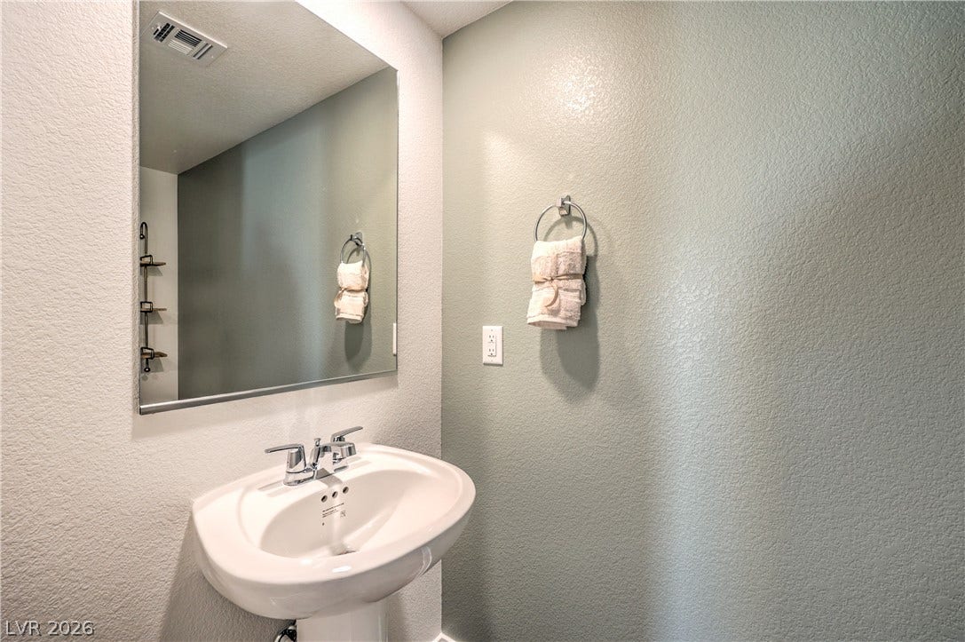 923 Black Heron Street, Henderson, NV 89011 A classic pedestal sink sits below a large wall mirror in this updated half bath.
