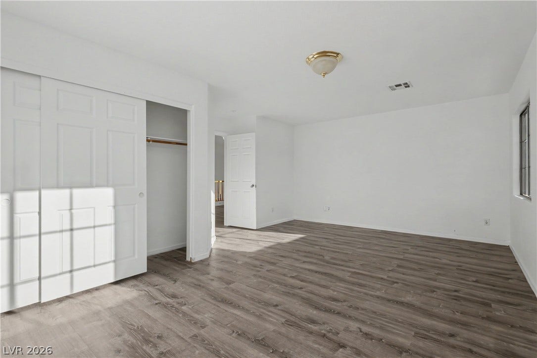 Rich wood-inspired flooring and crisp white walls define this airy, versatile bedroom space.