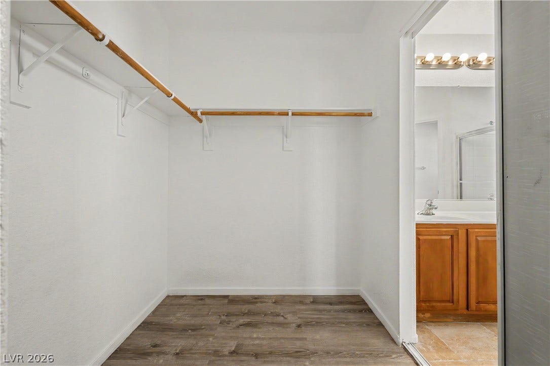 Generous closet space featuring built-in hanging rods and wood-look flooring connects directly to the bathroom.