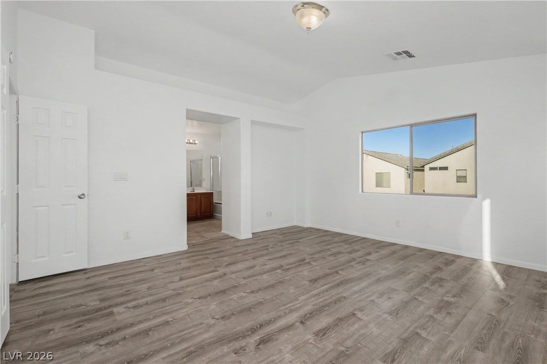A spacious bedroom features neutral walls, rich wood-look flooring, and a vaulted ceiling.
