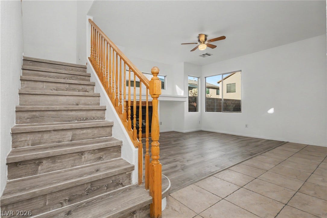An open living area features a wooden-railed staircase and a tile-to-wood floor transition.