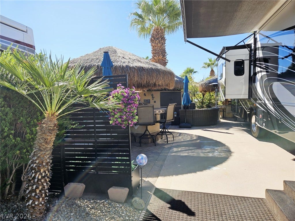 8175 Arville Street, #305, Las Vegas, NV 89139 Palm trees shade a paved patio featuring a built-in outdoor kitchen under a thatched palapa.