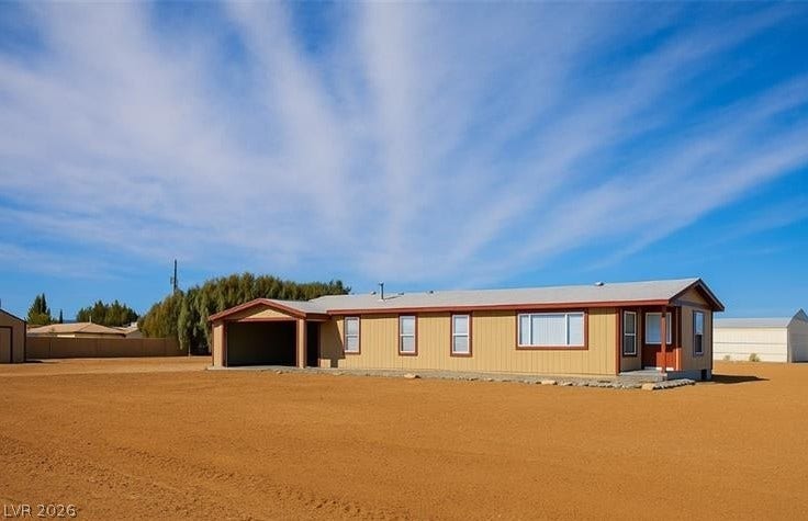 A single-story residence with an attached carport sits on a spacious desert lot under clear blue skies.