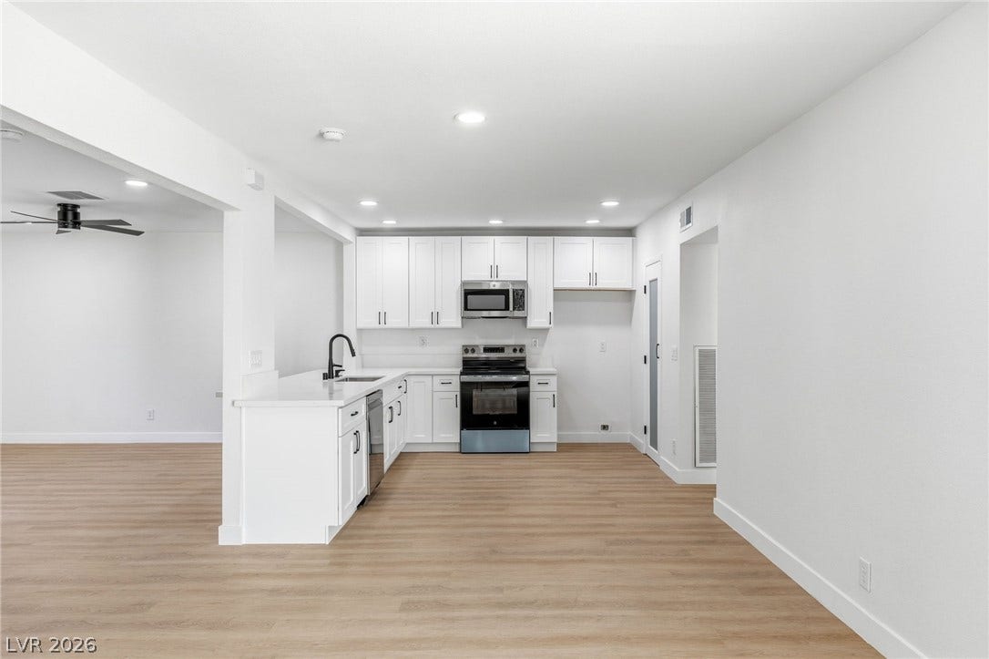 3471 One Nation Avenue, Las Vegas, NV 89121 A well-appointed kitchen features stainless steel appliances and abundant white cabinetry, seamlessly flowing into an adjacent living space.
