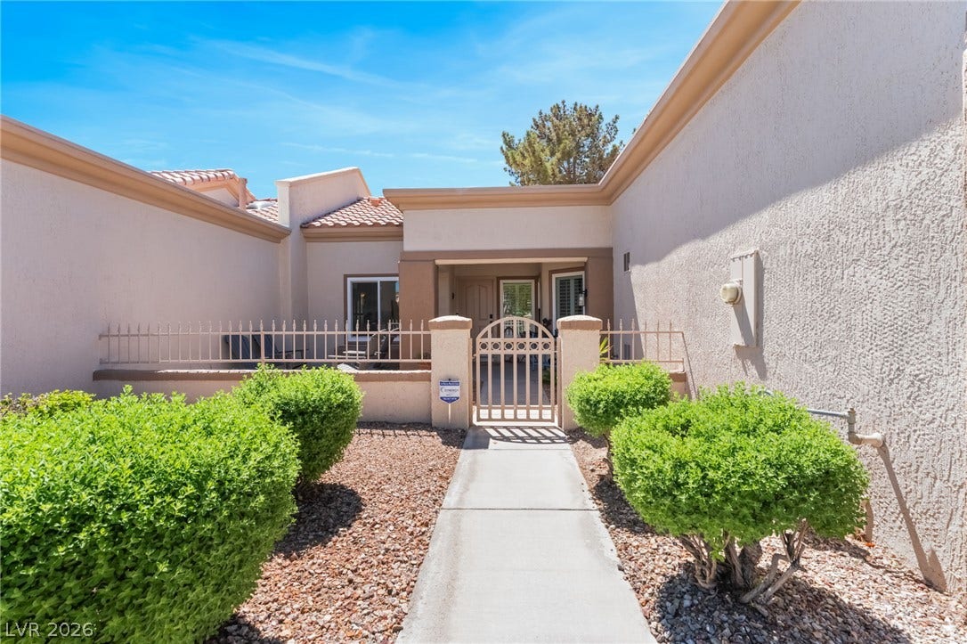 A concrete walkway leads through low-maintenance landscaping toward a private gated courtyard entrance.