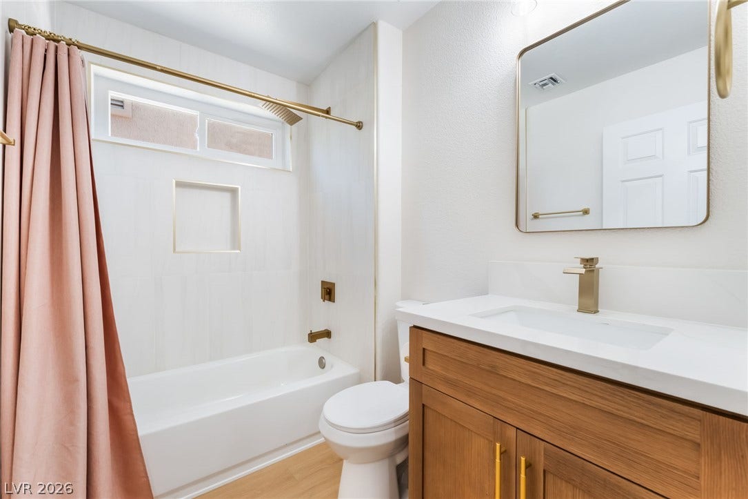 An elegant bathroom features a wood vanity, gold-toned hardware, and a tiled tub-shower combination.
