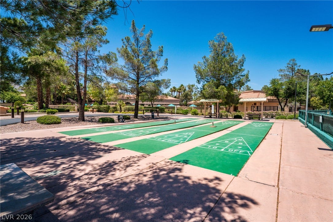 Lush trees surround the outdoor shuffleboard courts under a clear blue sky.