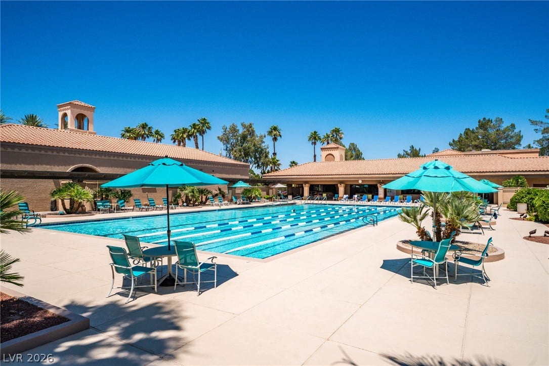 A spacious concrete deck surrounds this pristine outdoor lap pool under clear blue skies.