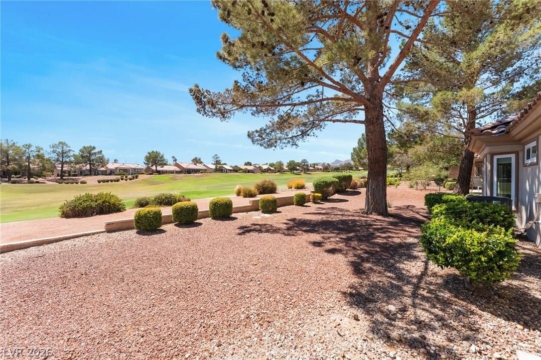 Mature trees shade a low-maintenance gravel yard overlooking rolling golf course fairways.
