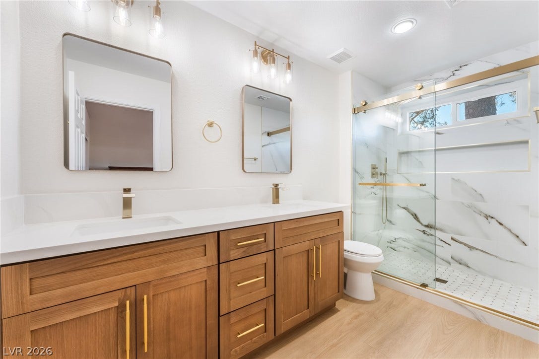 Warm wood cabinetry pairs with elegant stone countertops and a modern walk-in shower.
