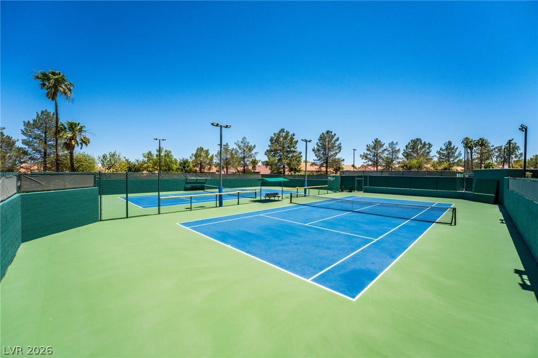 Professional-grade outdoor tennis courts sit under clear blue skies, surrounded by fencing.
