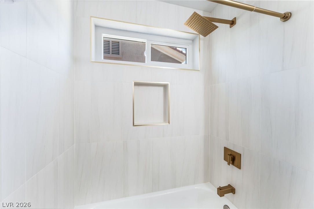Elegant gold hardware accents the modern tiled walls surrounding this pristine tub and shower combination.