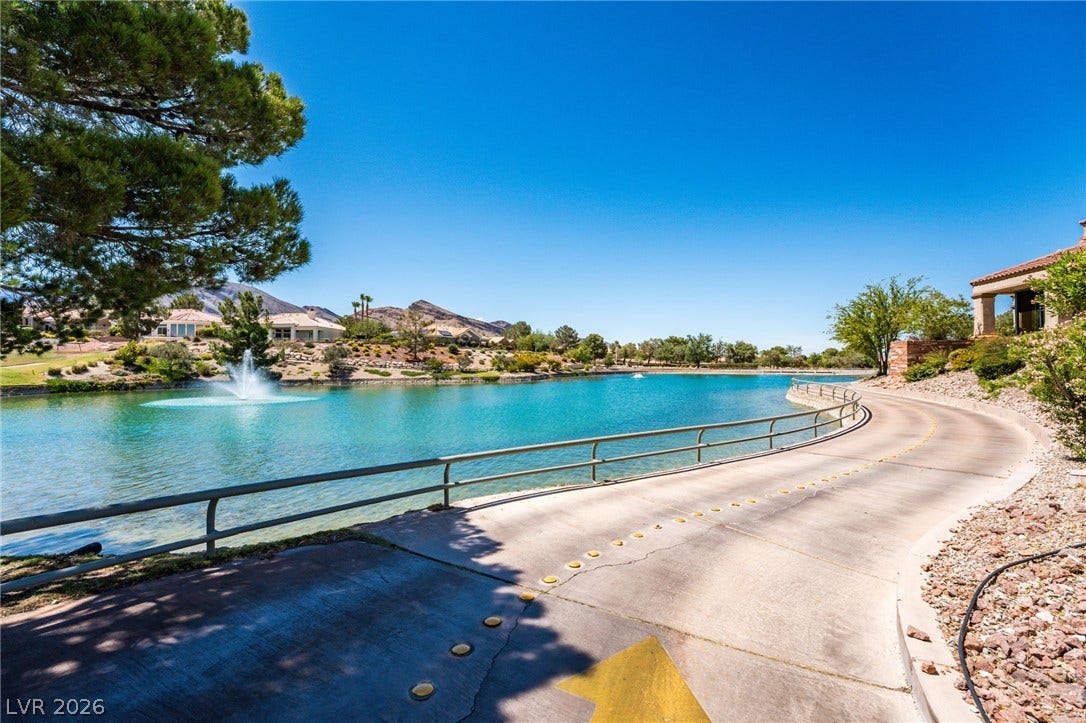 A paved path curves gracefully alongside a serene community lake under clear desert skies.