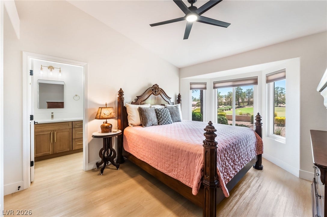 An elegant bedroom showcases warm wood flooring and a bay window overlooking manicured outdoor greenery.