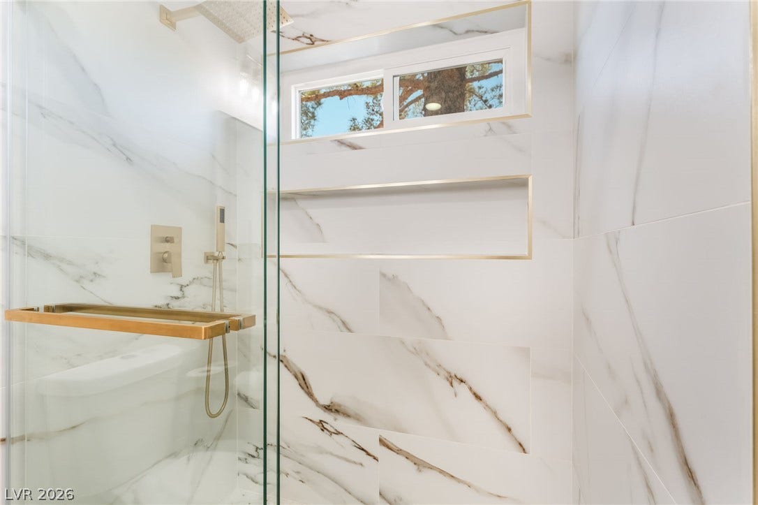 Gleaming marble-patterned tile surrounds a sleek walk-in shower featuring gold-toned fixtures.