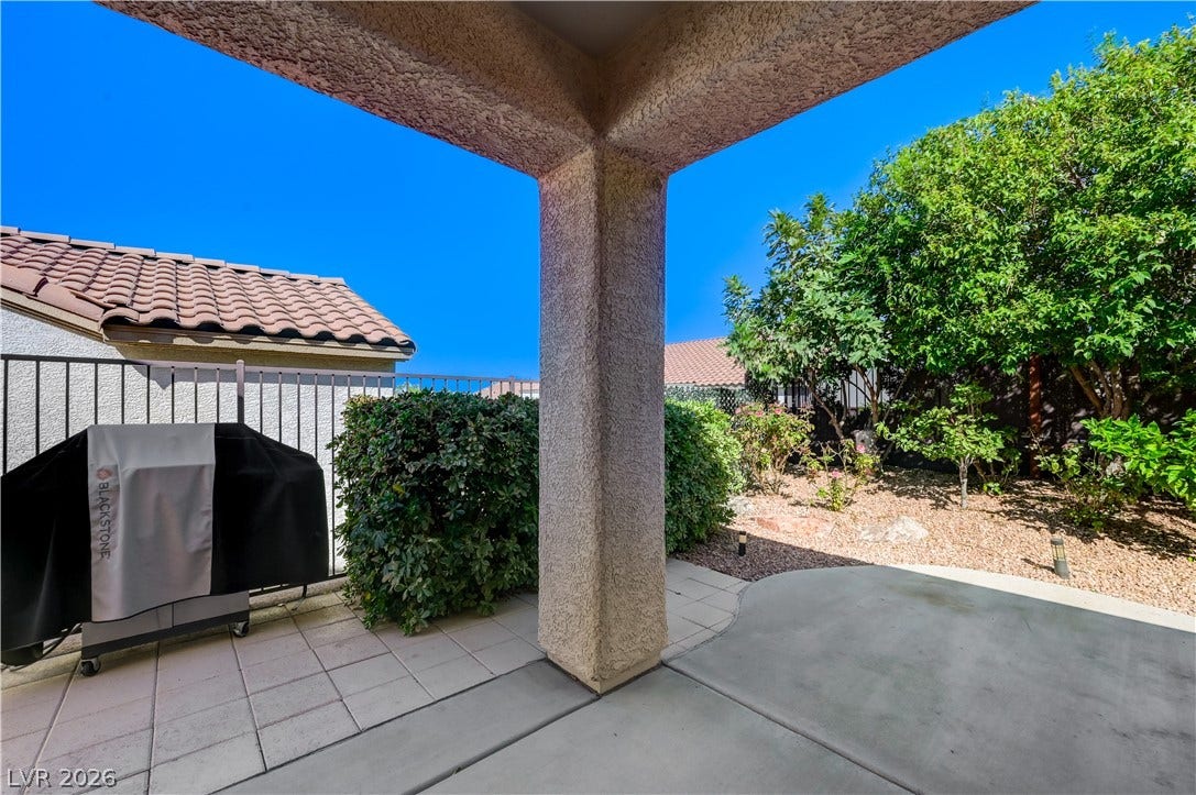 Shaded concrete patio looks out onto a low-maintenance gravel yard with mature green plantings.