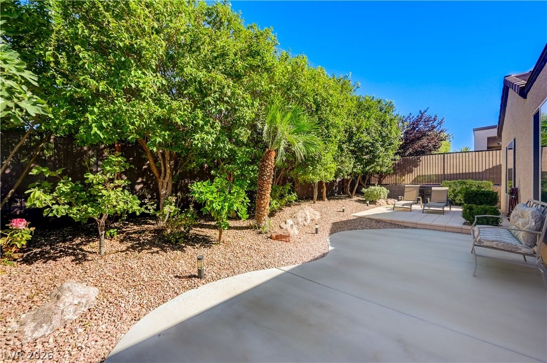 Mature trees and low-maintenance gravel landscaping border a spacious concrete patio area.