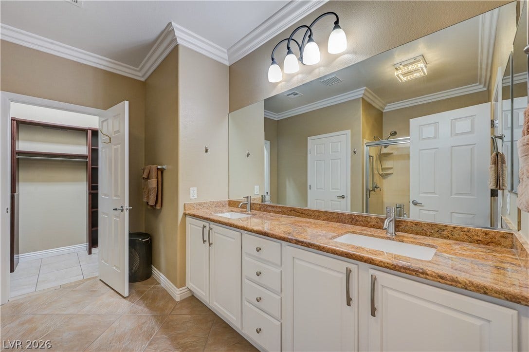 Ornate crown molding and polished stone countertops elevate this spacious dual-vanity washroom.