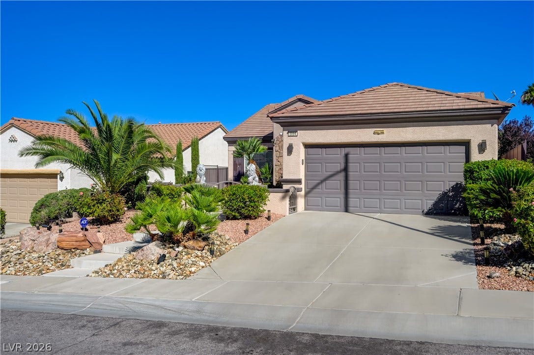 Manicured desert landscaping frames a concrete driveway leading to the spacious two-car garage.