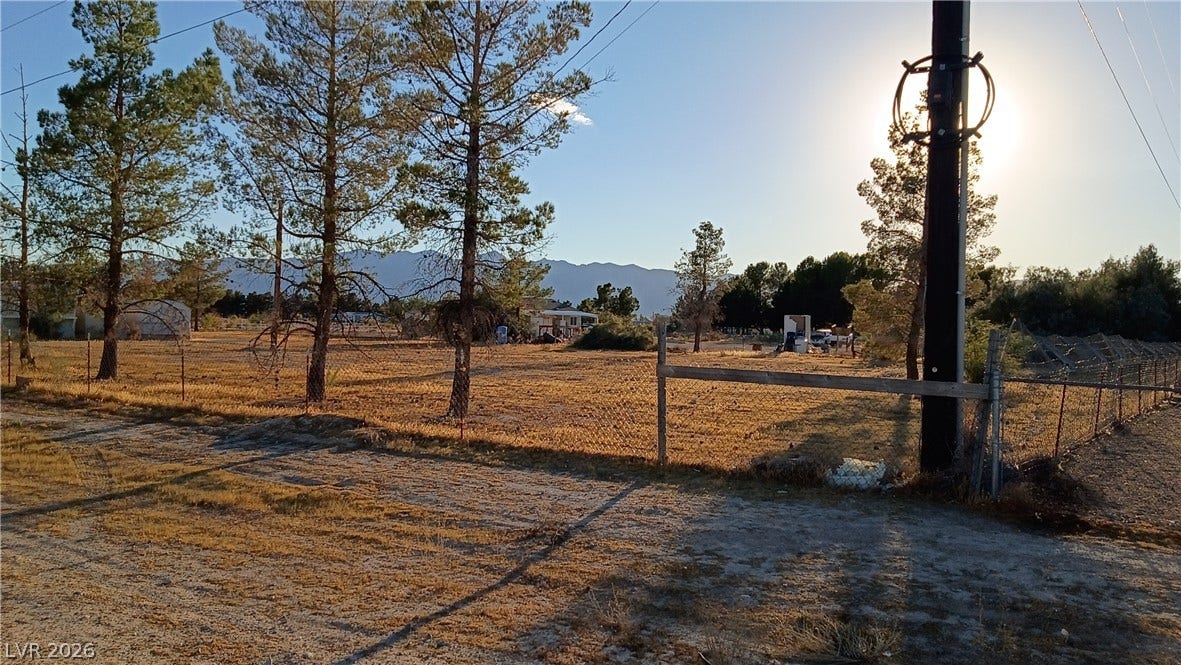 3490 E Savoy Boulevard, Pahrump, NV 89061 Mature trees frame the property line against a backdrop of distant mountains under clear skies.