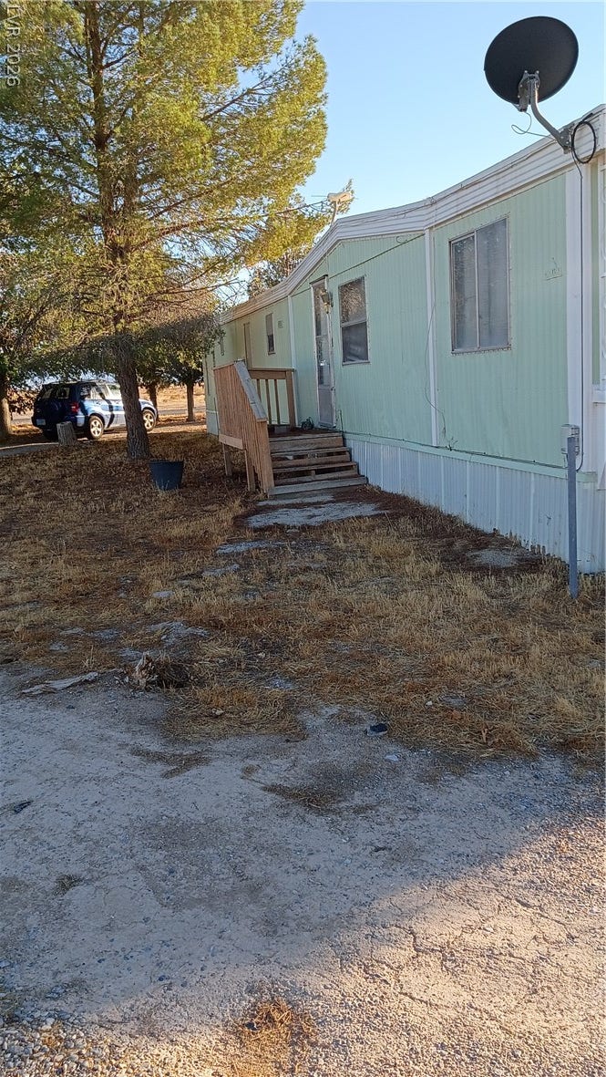 3490 E Savoy Boulevard, Pahrump, NV 89061 Mature trees frame the side of this manufactured home featuring simple wooden steps.