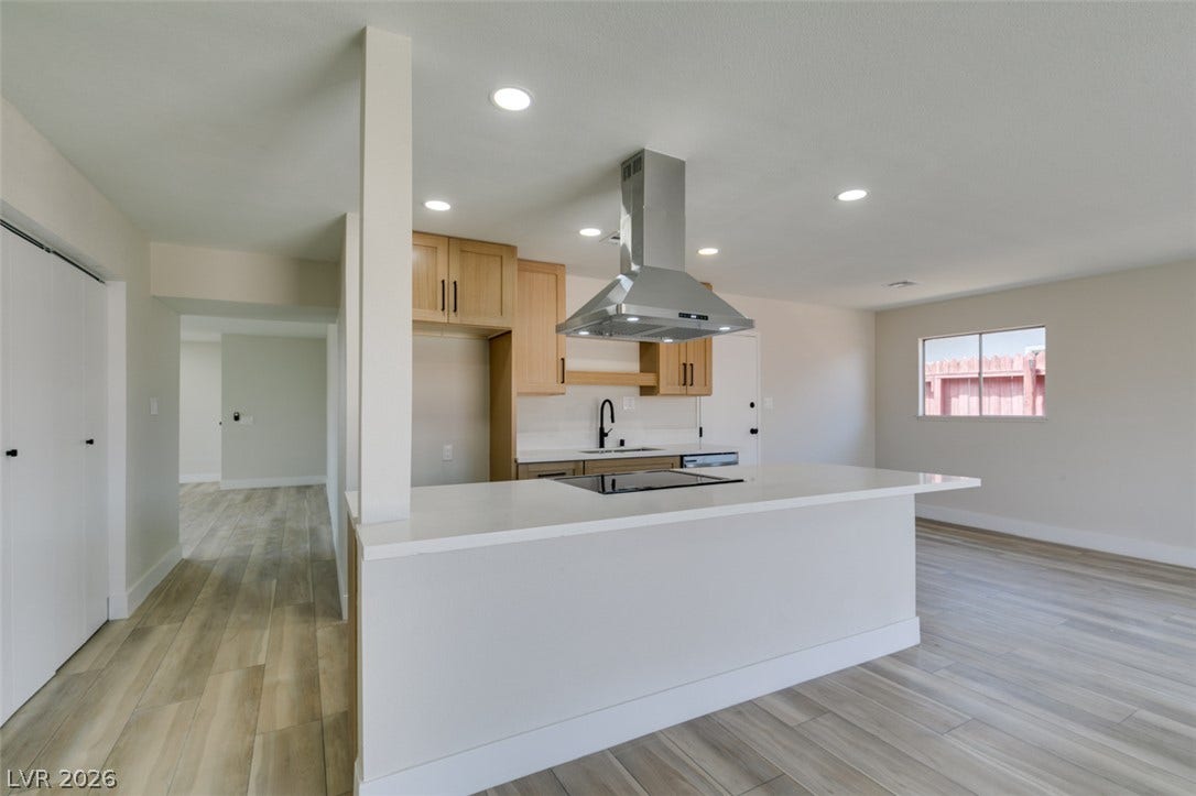 Smooth wood-look flooring stretches across this open layout featuring a modern peninsula kitchen.