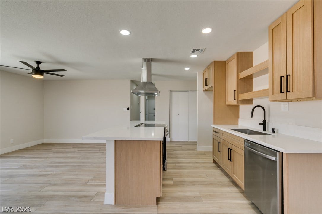 An open kitchen layout showcases sleek quartz countertops and warm wood cabinetry over plank flooring.
