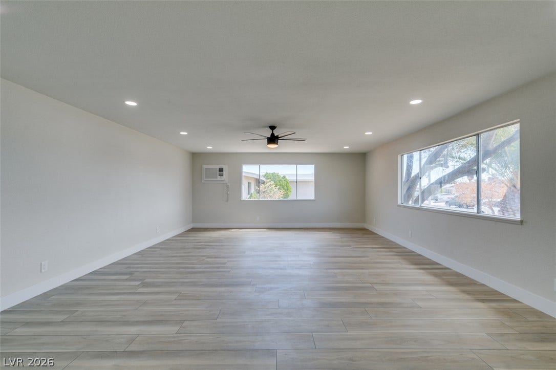 Recessed lighting illuminates this airy open space featuring wood-look flooring and multiple windows.