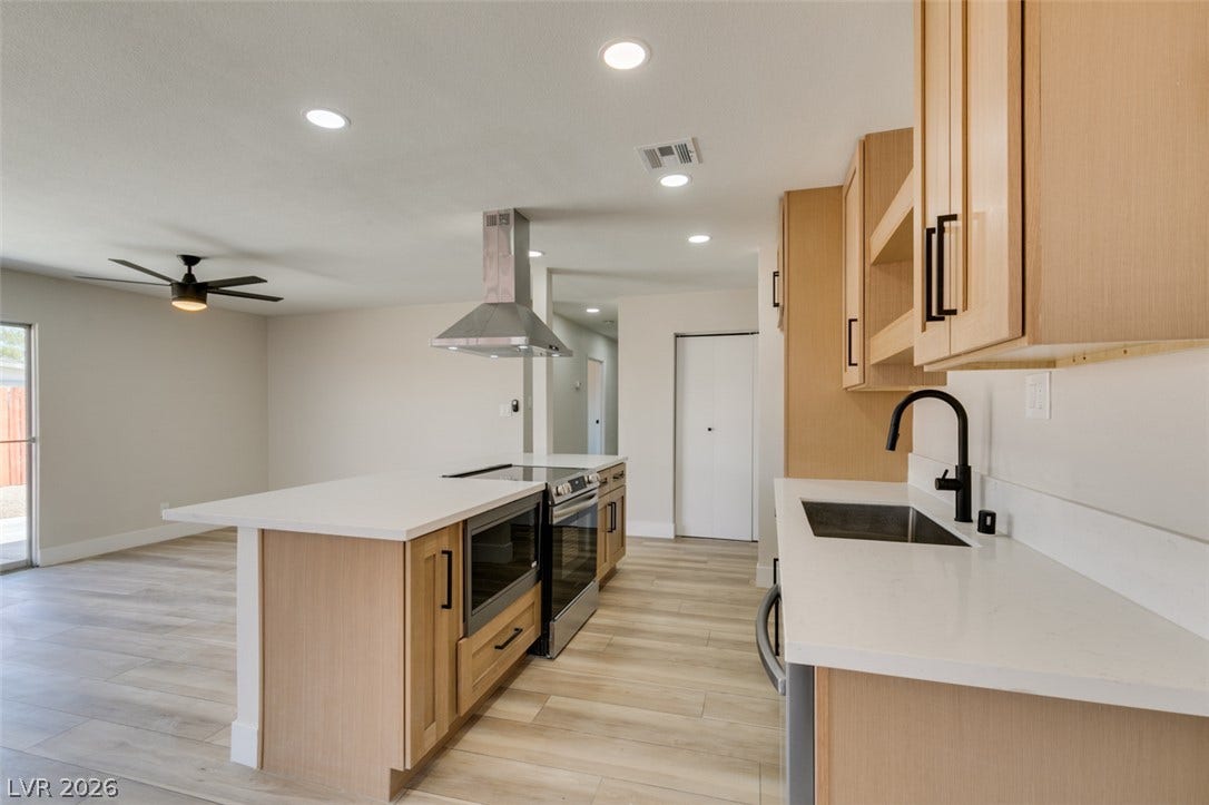 A spacious kitchen features a long central island, light wood cabinetry, and sleek solid-surface countertops.