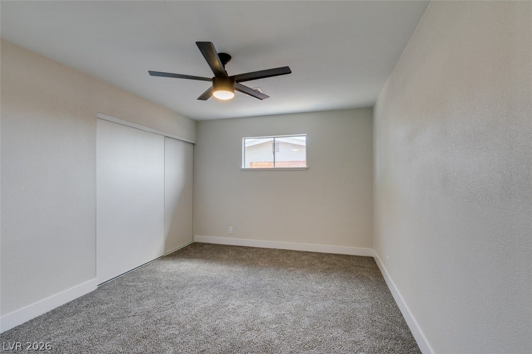 Plush carpeting anchors this versatile room under a smooth ceiling and simple window.