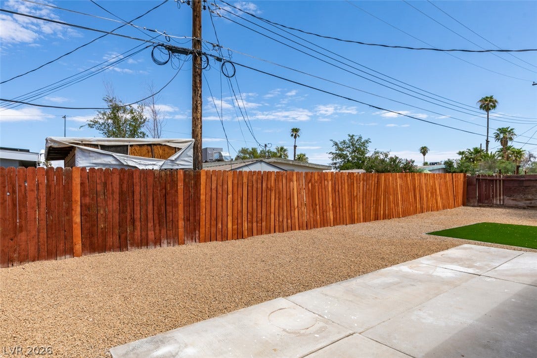 An expansive gravel yard features concrete pathways and a secure wood fence.