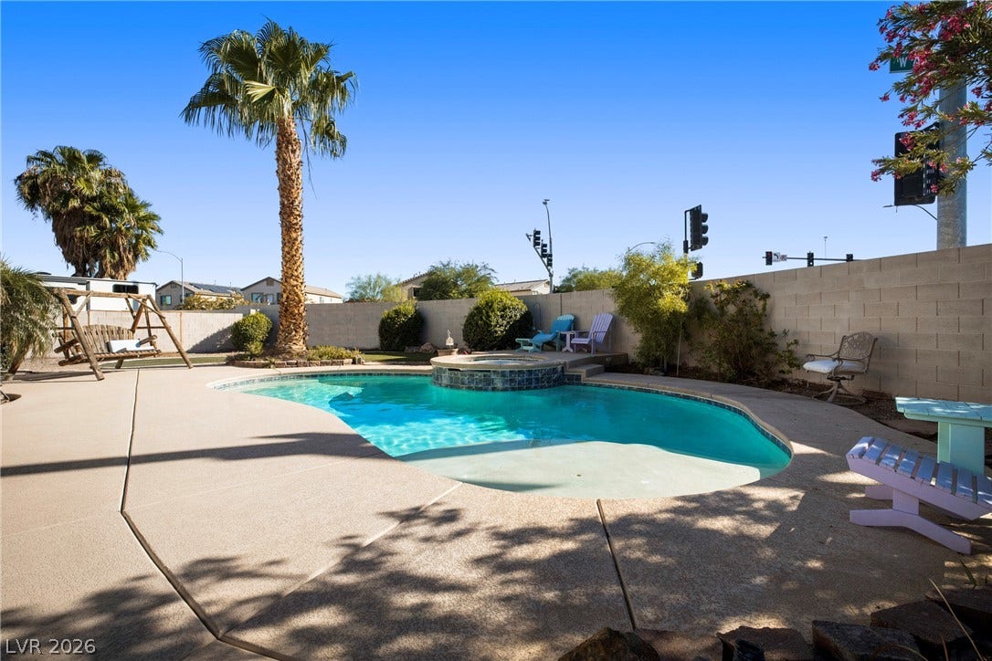 A sparkling swimming pool and integrated spa sit surrounded by a concrete patio.