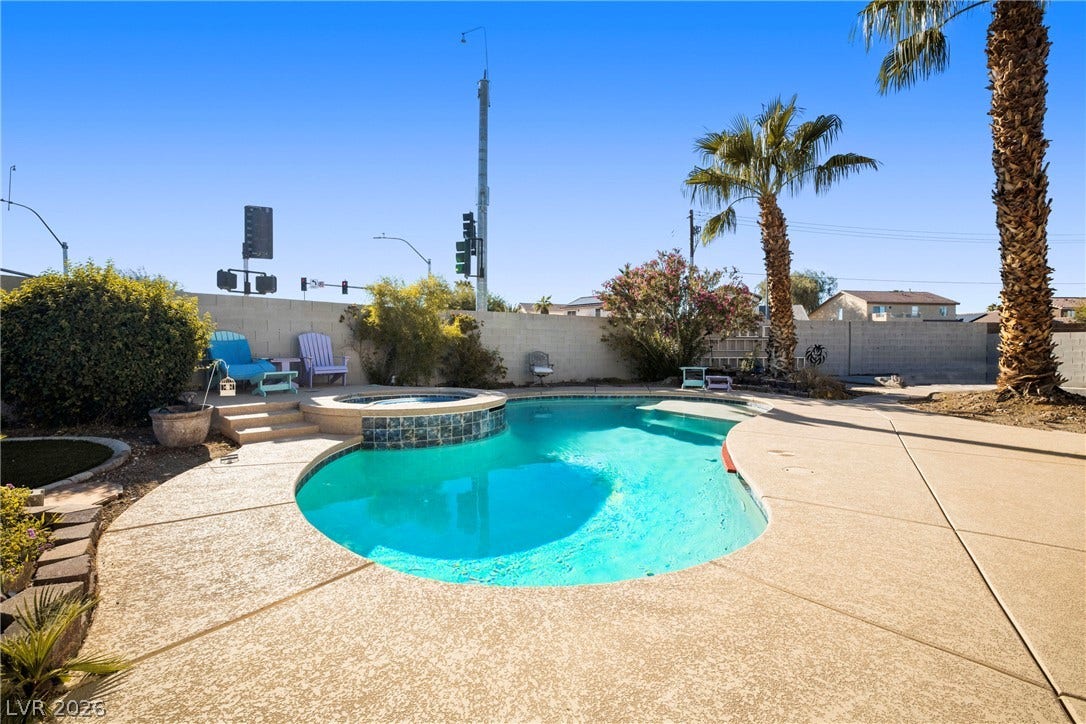 A sparkling in-ground pool and integrated spa sit surrounded by a concrete patio.