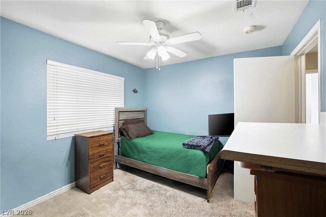 Soft wall tones complement carpeted flooring and large windows in this versatile secondary bedroom.