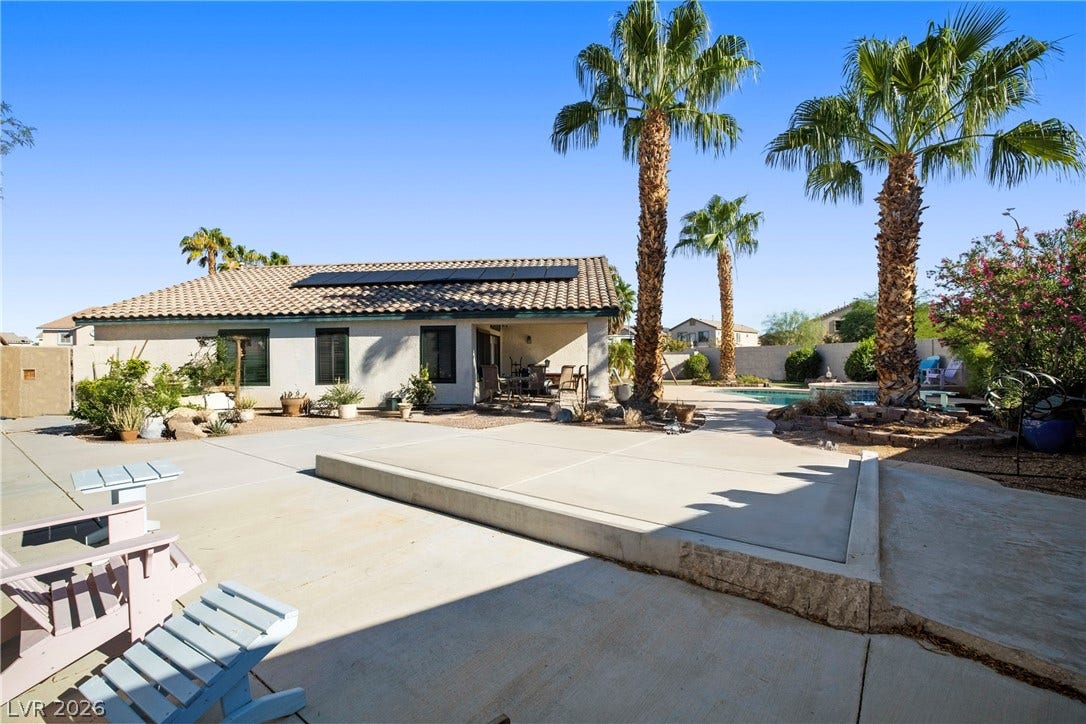 Soaring palm trees flank a spacious concrete patio overlooking the sparkling backyard pool.