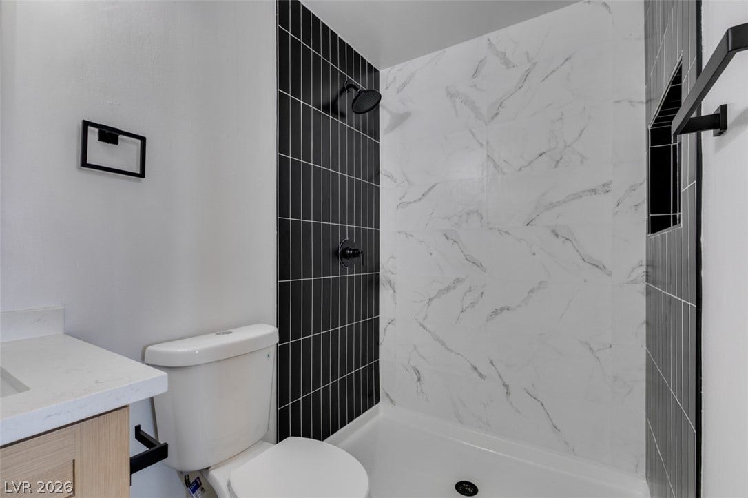 3638 Villa Knolls East Drive, Las Vegas, NV 89120 A modern shower stall features contrasting marble-patterned and dark vertical tiles alongside a clean vanity.