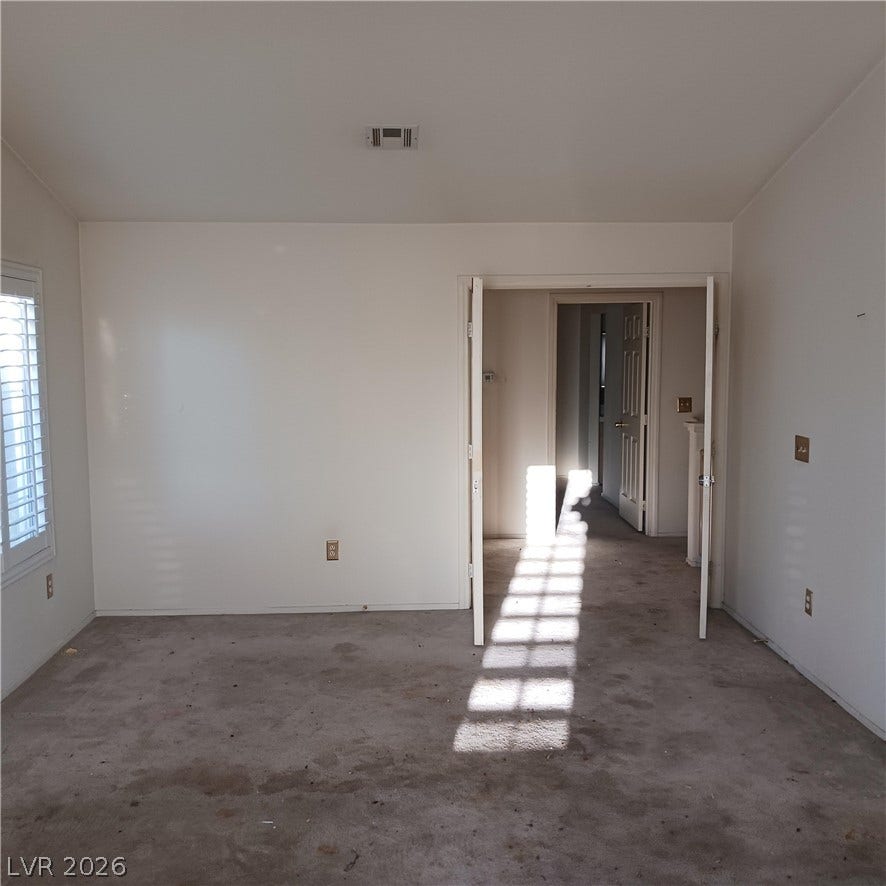 A spacious bedroom features neutral walls and double doors leading to the hallway.