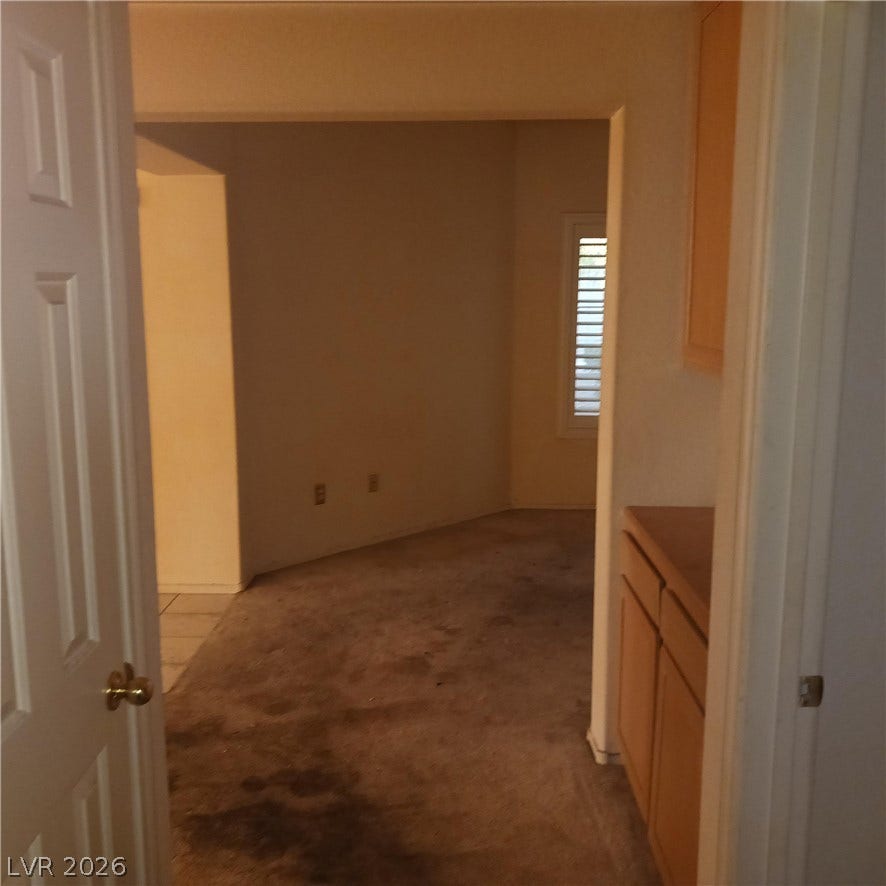An open doorway reveals a versatile living space featuring carpeted flooring and built-in cabinetry.