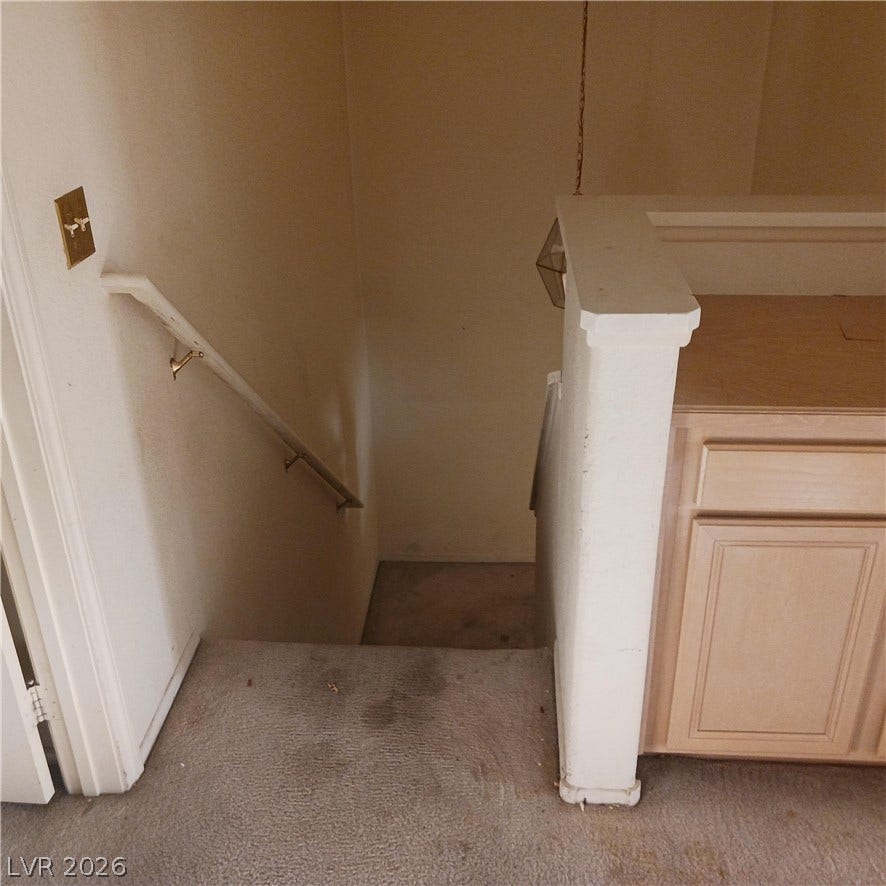 A carpeted staircase with a wooden handrail leads to the lower level of the home.
